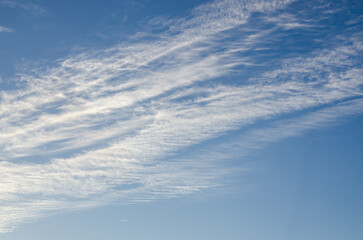 Wispy cirrus clouds drifting across a bright blue sky on a clear and sunny afternoon day © Andrii_Abriutin