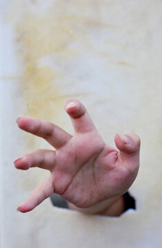 A hand with spread fingers in the broken hole.