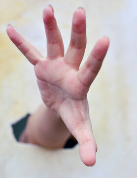 A hand with spread fingers in the broken hole.