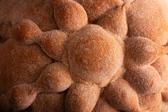 Macro close-up of traditional Mexican Pan de Muerto sweet bread texture, showing the detailed sugar-coated crust and bones shape dough for Day of the Dead.