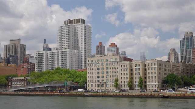 Apartment towers and prewar buildings line FDR Drive on the East River in New York City, New York, USA. Pedestrian bridge, green trees, yellow taxis and traffic under sunny summer clouds.