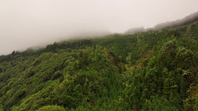 Aerial drone footage of misty fog rolling over lush green forest covered mountains on Sao Miguel Island in the Azores Portugal