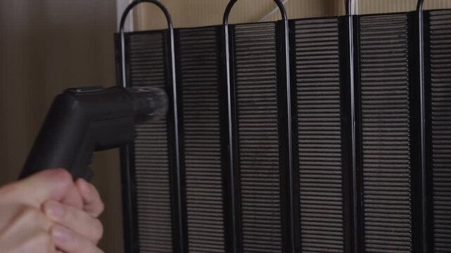 Professional technician using vacuum cleaner with brush nozzle for routine maintenance and cleaning of dusty condenser coils on back of household refrigerator. Concept of household chores.