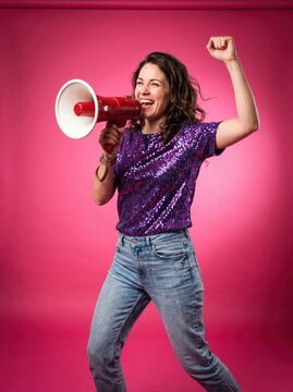 Woman cheering through megaphone with raised fist against pink studio backdrop. Activism, protest and public advocacy. Empowerment, confidence and self-expression.