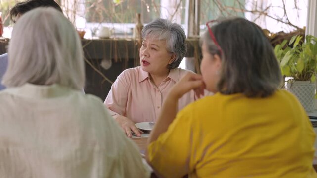 Gray haired senior woman speaks with friends across table during relaxed garden cafe reunion, enjoying meaningful companionship through friendship, togetherness, healthy aging outdoors.