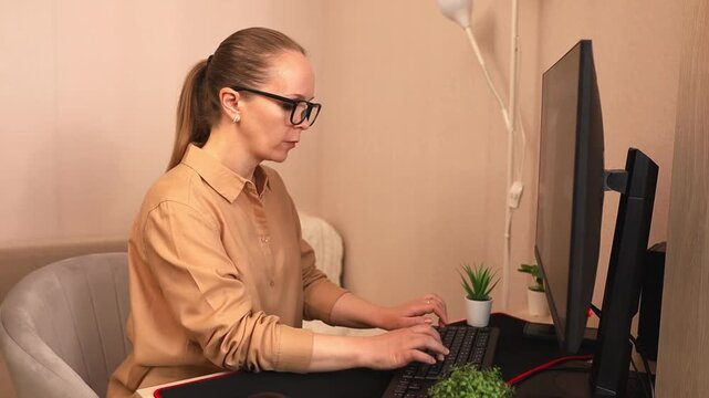 A focused young white woman with glasses is working on a computer at her desk.
