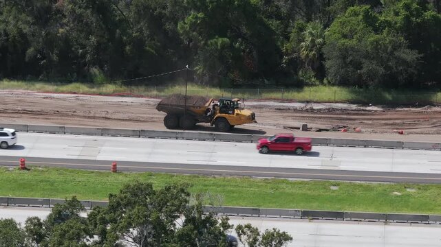 Earthmover truck driving in reverse on adjacent construction highway expansion site