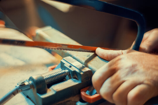 Close-up of a hand using a hacksaw to cut a metal piece clamped in a vise. Authentic metalworking photo for industrial, craft and maker projects