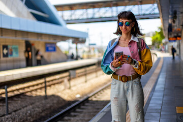 Railway theme. A beautiful young woman with a backpack holds a phone in her hand and waits for a train, standing on the platform. Tel Aviv, Israel. © zhukovvvlad
