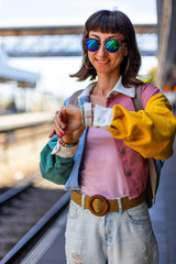 A young woman checks the time on her smartwatch at the train station. Railway theme. A beautiful young woman in sunglasses stands on the platform. Tel Aviv, Israel. © zhukovvvlad