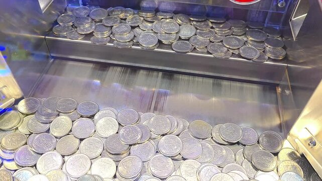 Close up view of silver metallic game tokens moving on shelf inside coin pusher arcade machine at amusement center
