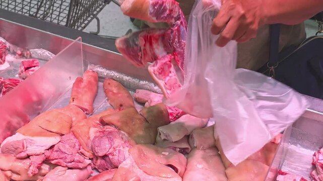 selecting fresh raw pork trotters offal cut into clear plastic bag at Asian supermarket meat counter
