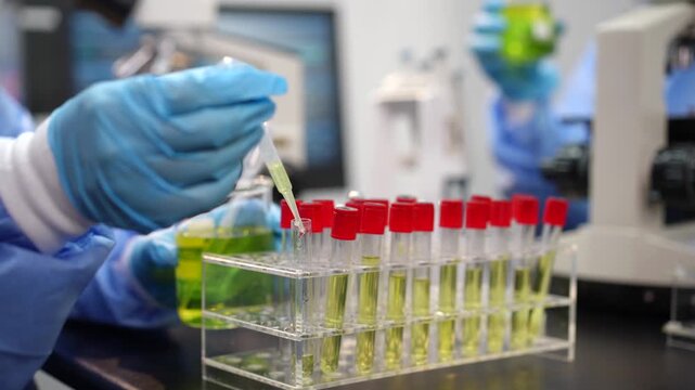 Scientist wearing blue gloves uses a pipette to add liquid samples into red-capped test tubes in a modern laboratory.