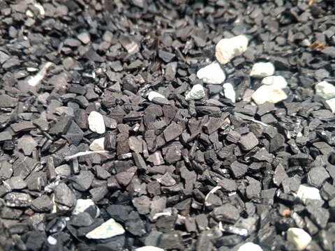 Close-up view of dark crushed stones and gravel mixed with scattered white rocks, creating a rough natural ground texture suitable for construction, landscaping, and abstract background concepts