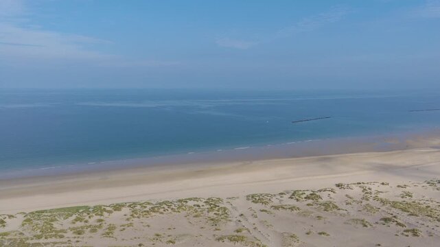 Aerial view flying over dunes and beach grass above calm sea towards a canal, Dunkirk coast, northern France