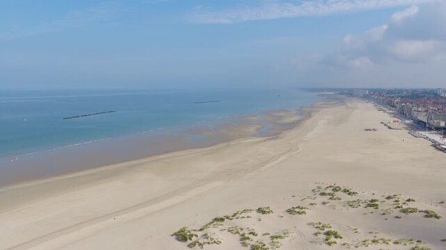 Aerial view of a wide empty sandy beach with calm sea and dunes under a hazy blue sky, Dunkirk coast, northern France