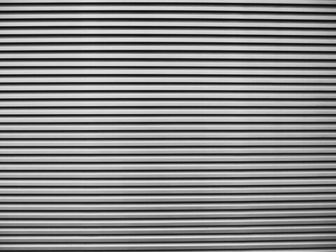 textured surface of tightly spaced, horizontal metal or plastic slats, creating a repeating linear pattern with alternating light surfaces and dark shadows
