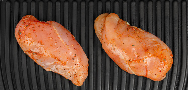 Two seasoned raw chicken breast fillets arranged on a black ridged grilling surface viewed from above for food preparation imagery