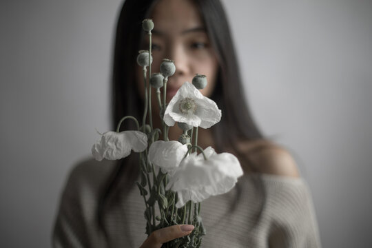 Southeast Asian woman holding white poppy flowers with seed pods