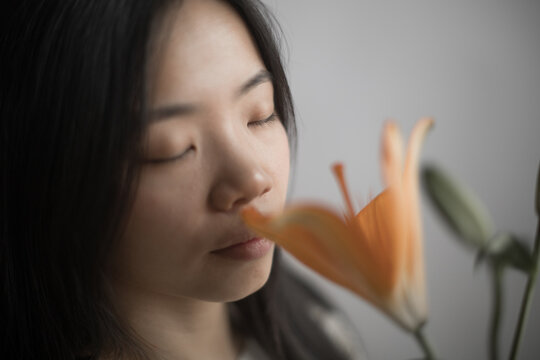 Southeast Asian woman with closed eyes smelling orange lily flower