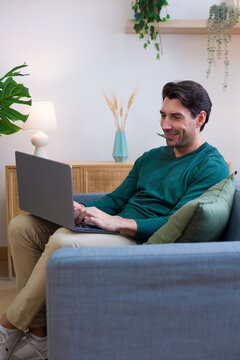 White man using laptop sitting on sofa in home living room