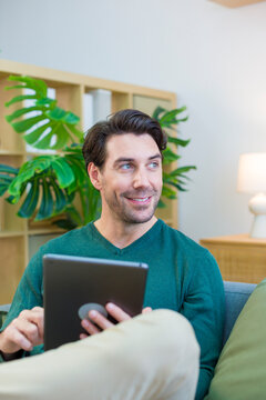 White man sitting on couch using tablet in living room