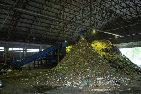 Heavy excavator loading piles of municipal solid waste onto an industrial trommel screen conveyor system inside