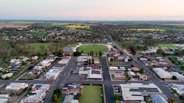 Aerial drone view of the town of Bordertown, South Australia, with a grid of streets, shops and commercial buildings, a sports oval complex, houses among trees, and flat farmland with crop fields