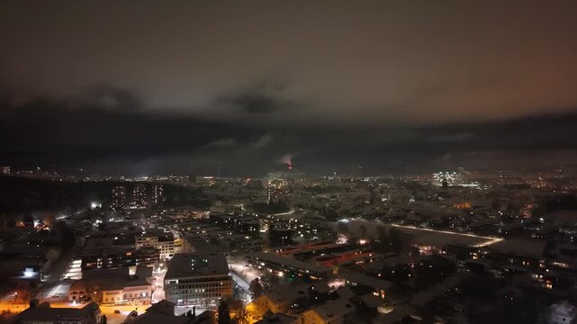 Night drone flight over the lights of the suburbs of Berne, Switzerland on a mystic winter night all covered with snow.
