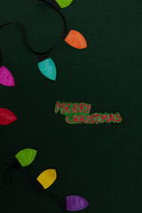 Merry Christmas message next to a colorful paper Christmas light garland on a dark green background, a graphic resource for holiday greetings and festive designs, with all elements made of paper © Answer 7
