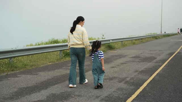 mother and preschool child girl holding hand and walking on a road on mountain in the morning