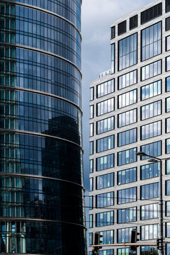 Curved glass office tower and rectangular facade forming a narrow architectural canyon in Wola Warsaw with contrasting window grids and blue reflections