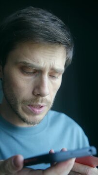 Man holding smartphone reading credit card numbers to unknown caller unaware of financial fraud. Deception, data theft, scam concept. Man reading credit card numbers to phone scammer without realizing