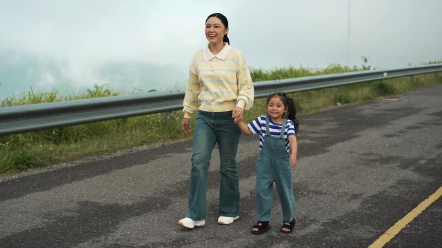 mother and preschool child girl holding hand and walking on a road on mountain in the morning