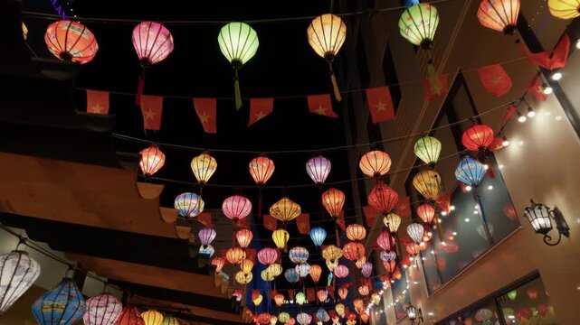 Colorful hanging paper lanterns over narrow urban pedestrian street at night with warm festive glow and diagonal perspective