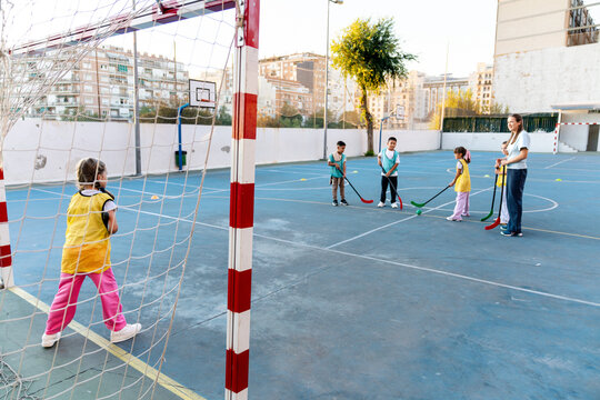 Young students playing floorball on outdoor court during physical education class, practicing sport and teamwork with instructor