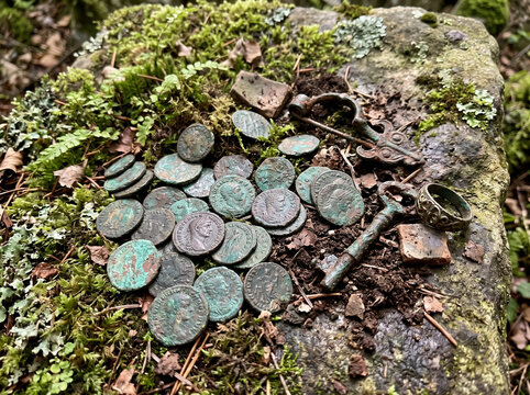 Ancient Roman coins hoard unearthed with jewelry and key on mossy stone by metal detectorist