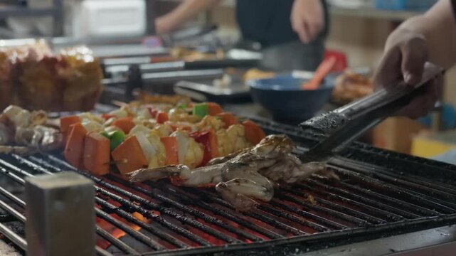 Low-angle close-up showing hands using tongs to brush glazed meat and bell pepper onion skewers over glowing charcoal embers
