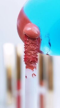 Red liquid flowing from the tip of a brush. Extreme close up view of brush coated with red liquid. Isolated on soft white background. Makeup product concept.