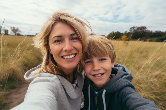 Happy mother and young son bonding during an outdoor autumn adventure, capturing a close up selfie in a sunlit field, reflecting genuine smiles and a strong family connection