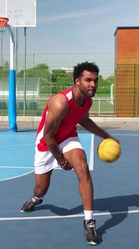 Young man in sportswear dribbling a basketball on an outdoor court. Skillful player practicing his moves with concentration and smiling