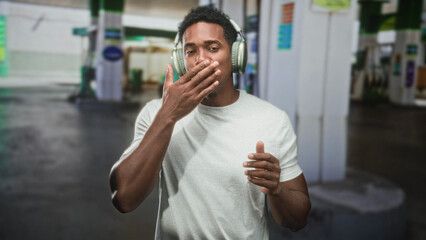 Black man wearing headphones dancing and smiling with hands raised at a street gas station  joy music energy. © Krakenimages.com