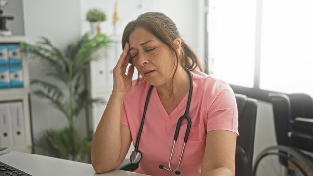 Woman doctor with stethoscope removing glasses and massaging temples at desk in building; compassion fatigue.