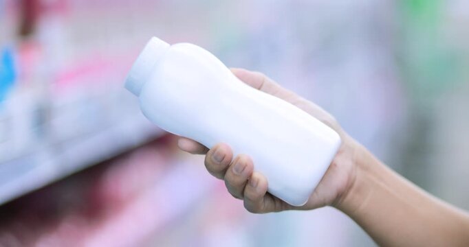 Customer holding a blank white plastic powder bottle while examining a sample product in store, Shopping in a store, Baby powder testing, Hygiene, Retail shopping, Personal care, consumer choice