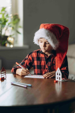 Boy in Santa hat writes a Christmas letter at home