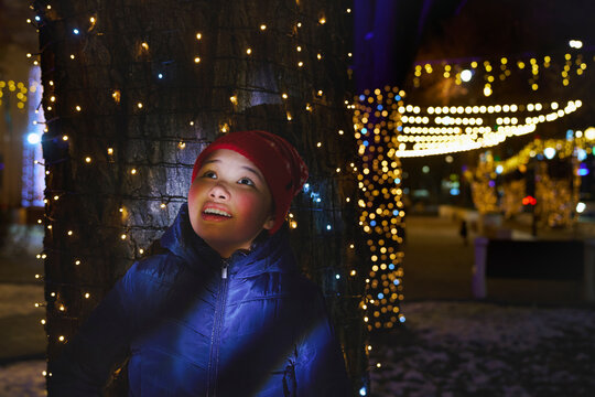 Happy girl in winter coat admires Christmas light outdoors at night