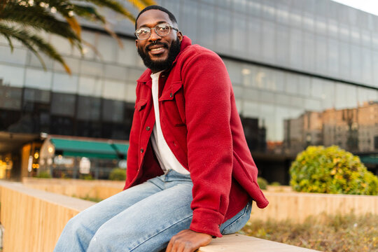 Man in red jacket sitting outdoors in urban city environment