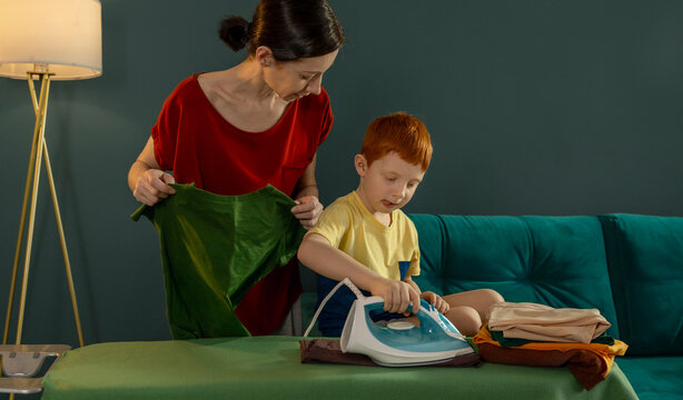 Mother and son ironing clothes together at home in the evening