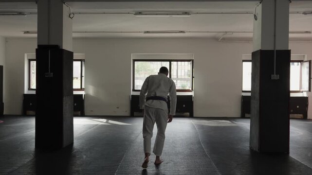 Man in martial arts uniform kneeling and performing a formal bow zarei on the floor of training gym