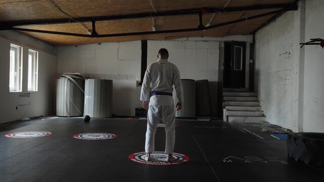 Person wearing white martial arts uniform standing on circular marker indoor training gym dojo